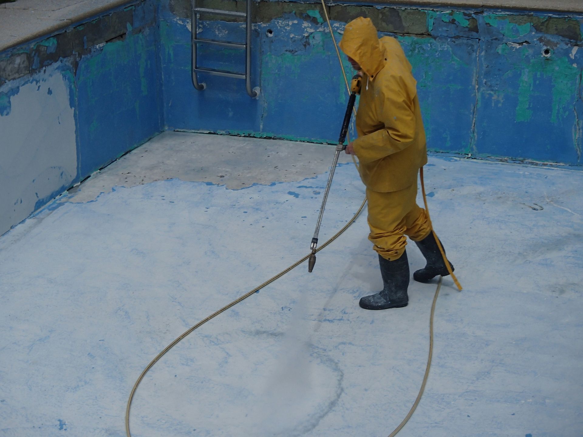 A man in a yellow suit is cleaning a swimming pool with a pressure washer.
