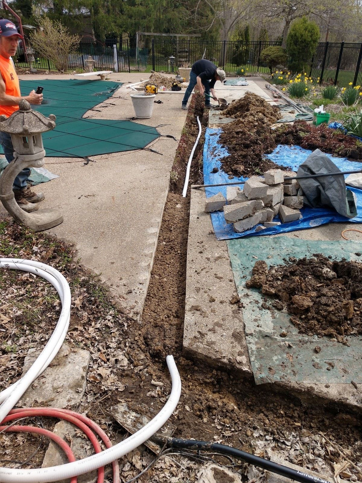 A man is digging a hole in the ground next to a hose.