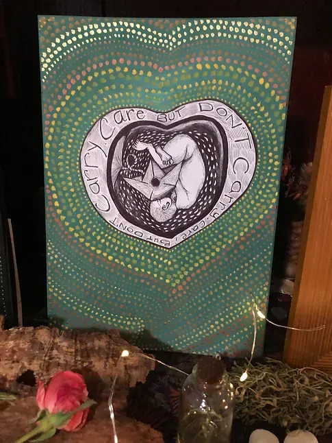 A drawing/painting of a baby curled up with a paper boat, a symbol of both grief and joy to me, surrounded by a growing heart with the words: care but don't carry. Created with black pen and green, yellow and orange paint.