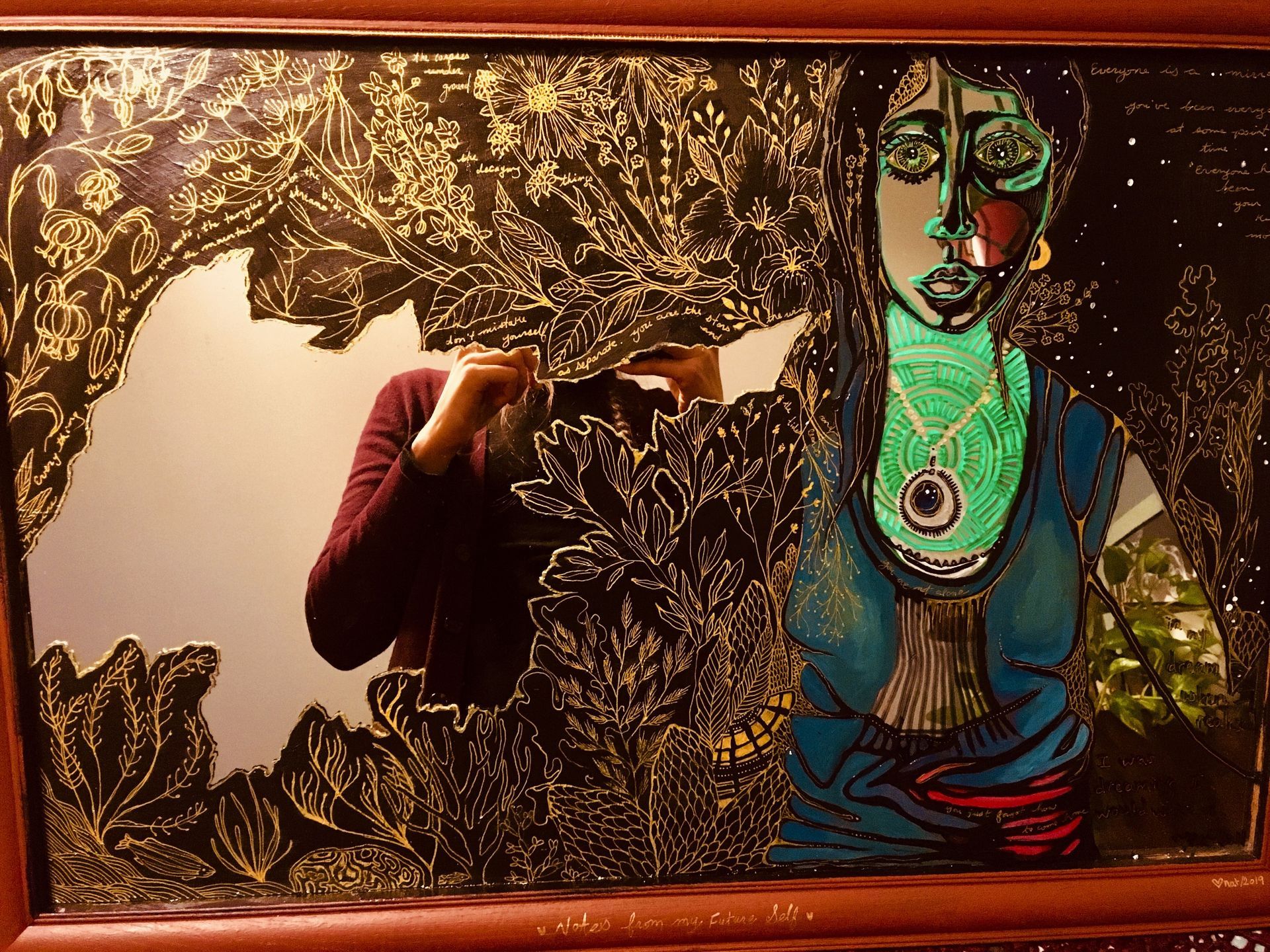 A painting of a woman with a vibrant heart-space, her arms outstretched, turning into both earth and sea plants (black and gold).