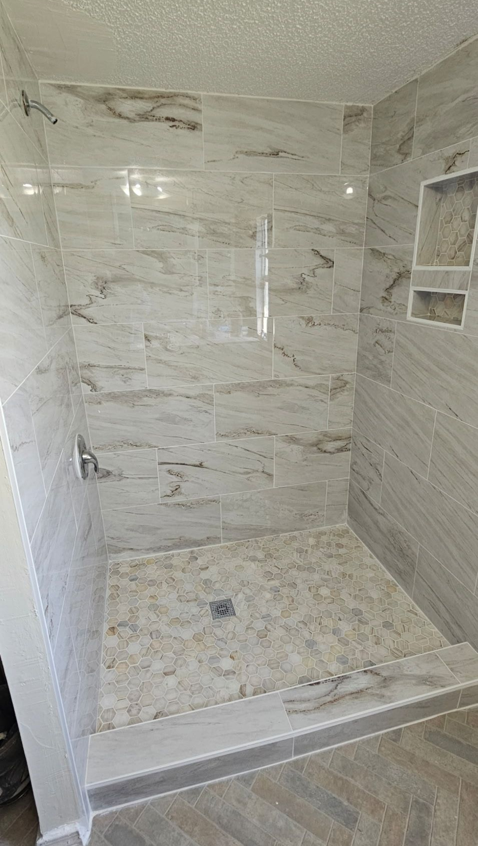 Tiled shower with pebble floor, built-in shelves, and a silver shower head. Walls have marble-like pattern.
