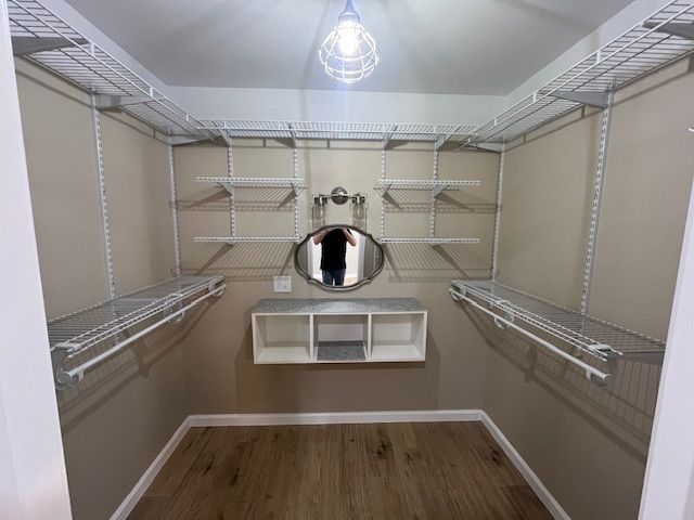 Empty walk-in closet with wire shelving, a small vanity, and an oval mirror, under a single light fixture.