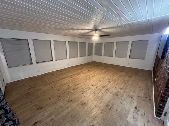 Empty room with wood-look floor, white walls, screened windows, and a ceiling fan.