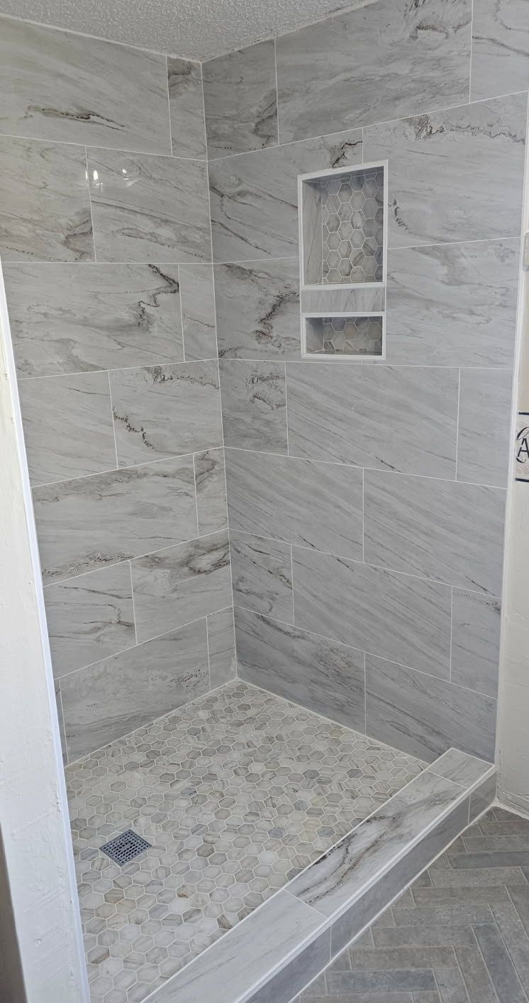 Gray tiled shower with built-in shelf and granite-like floor.