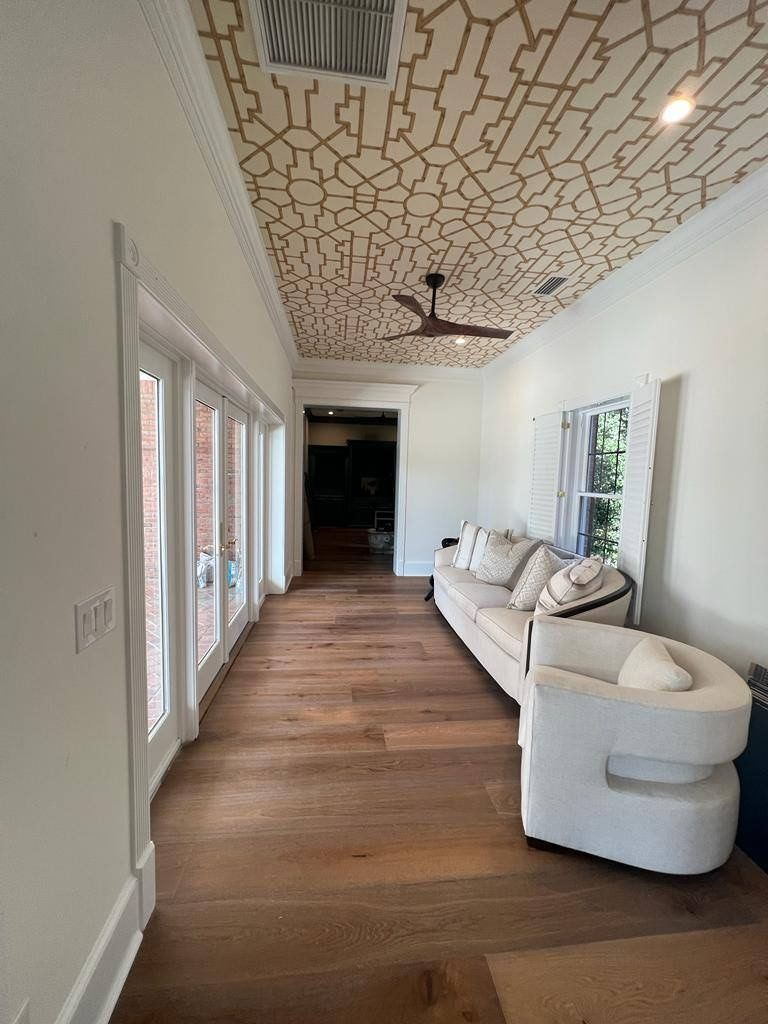 Narrow room with wood floor, white walls and trim, patterned ceiling. A sofa and chair sit along the wall.
