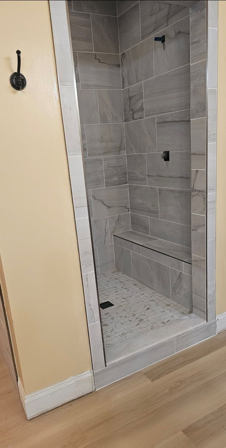 Walk-in shower with gray tile walls, built-in bench, and terrazzo floor.