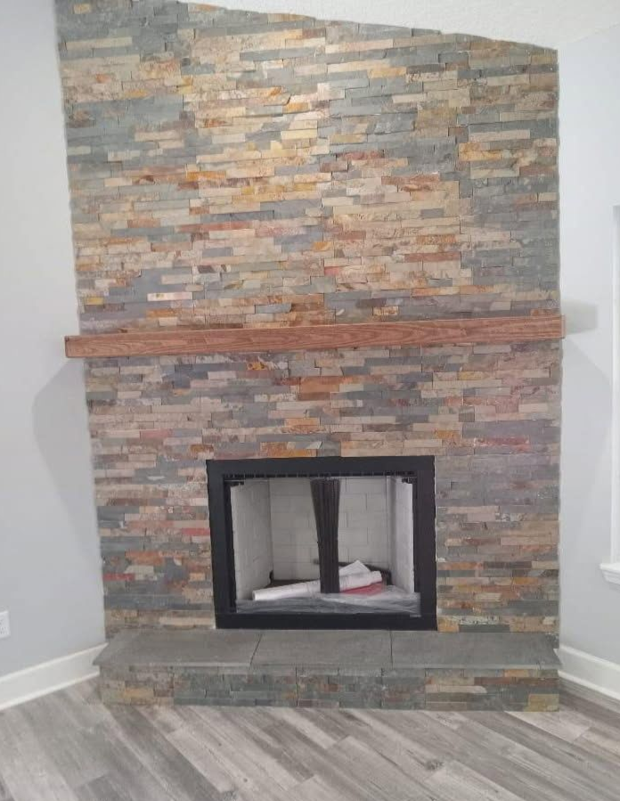 Fireplace with stacked stone facade and wood mantel. Black framed firebox.