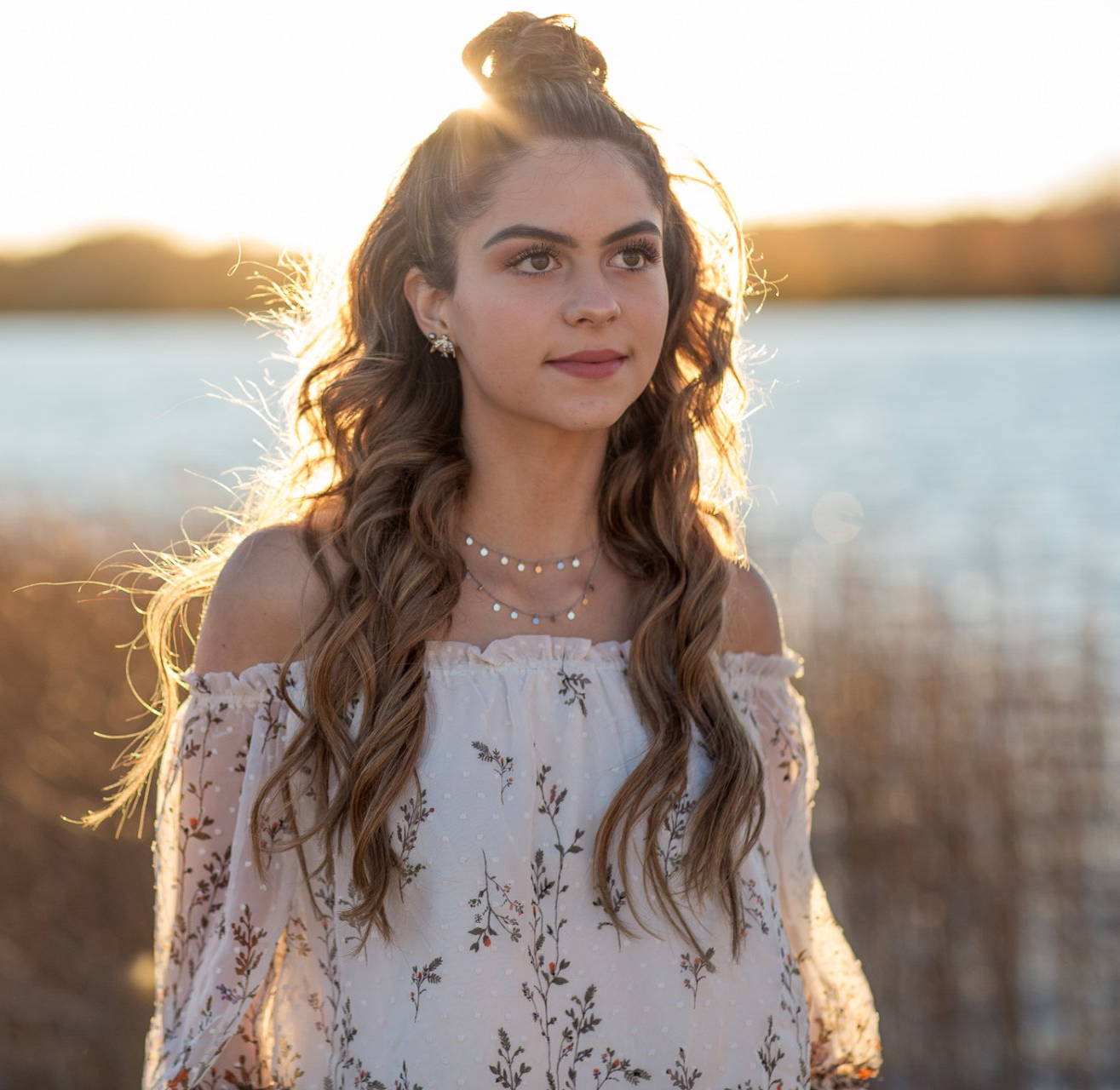 A woman in a white dress is standing in front of a body of water.