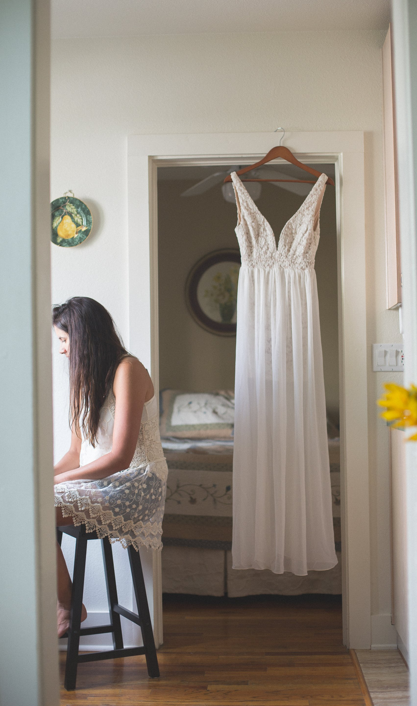 A woman is sitting at a table in front of a white dress hanging on a hanger.