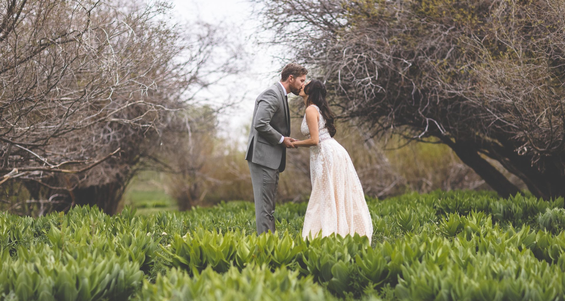 A bride and groom are kissing in a field of trees.
