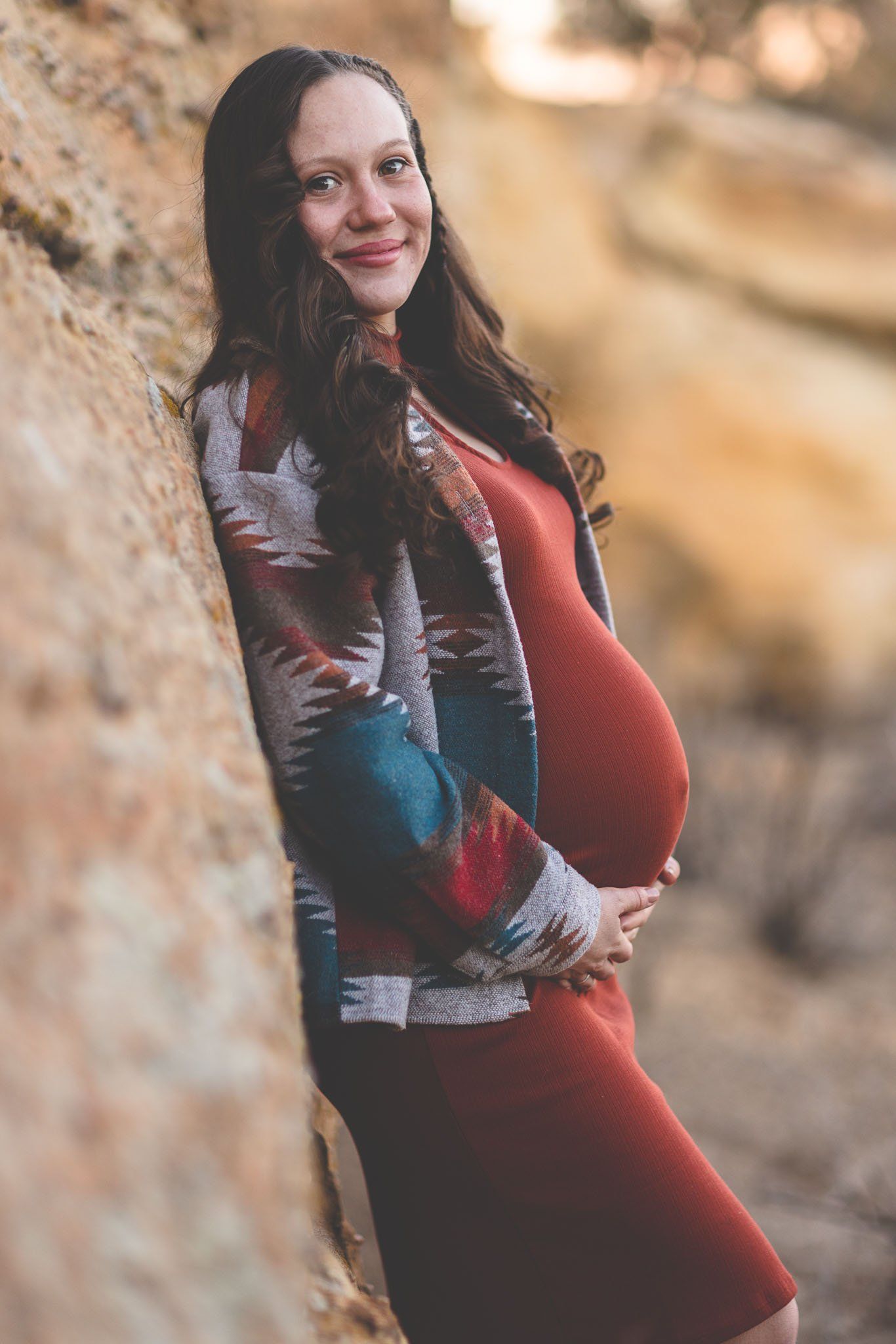 A pregnant woman is leaning against a rock while holding her belly.