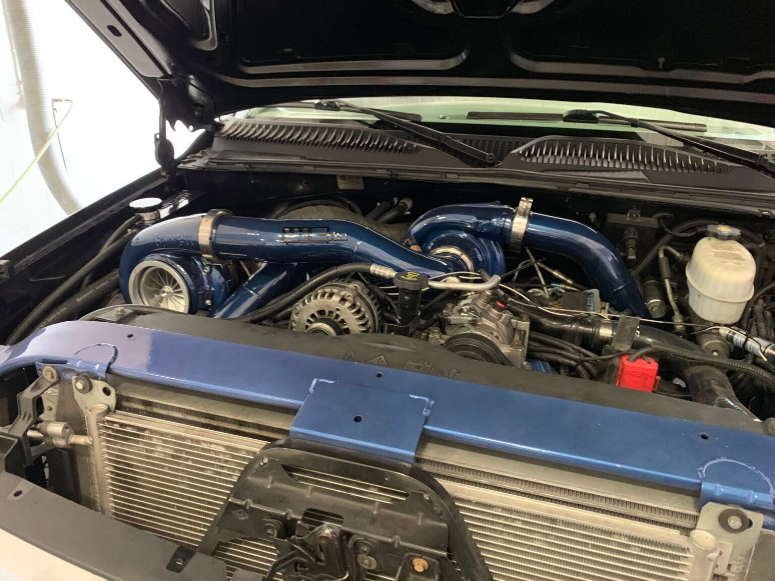 Car engine bay with blue intake pipes and exposed components under an open hood