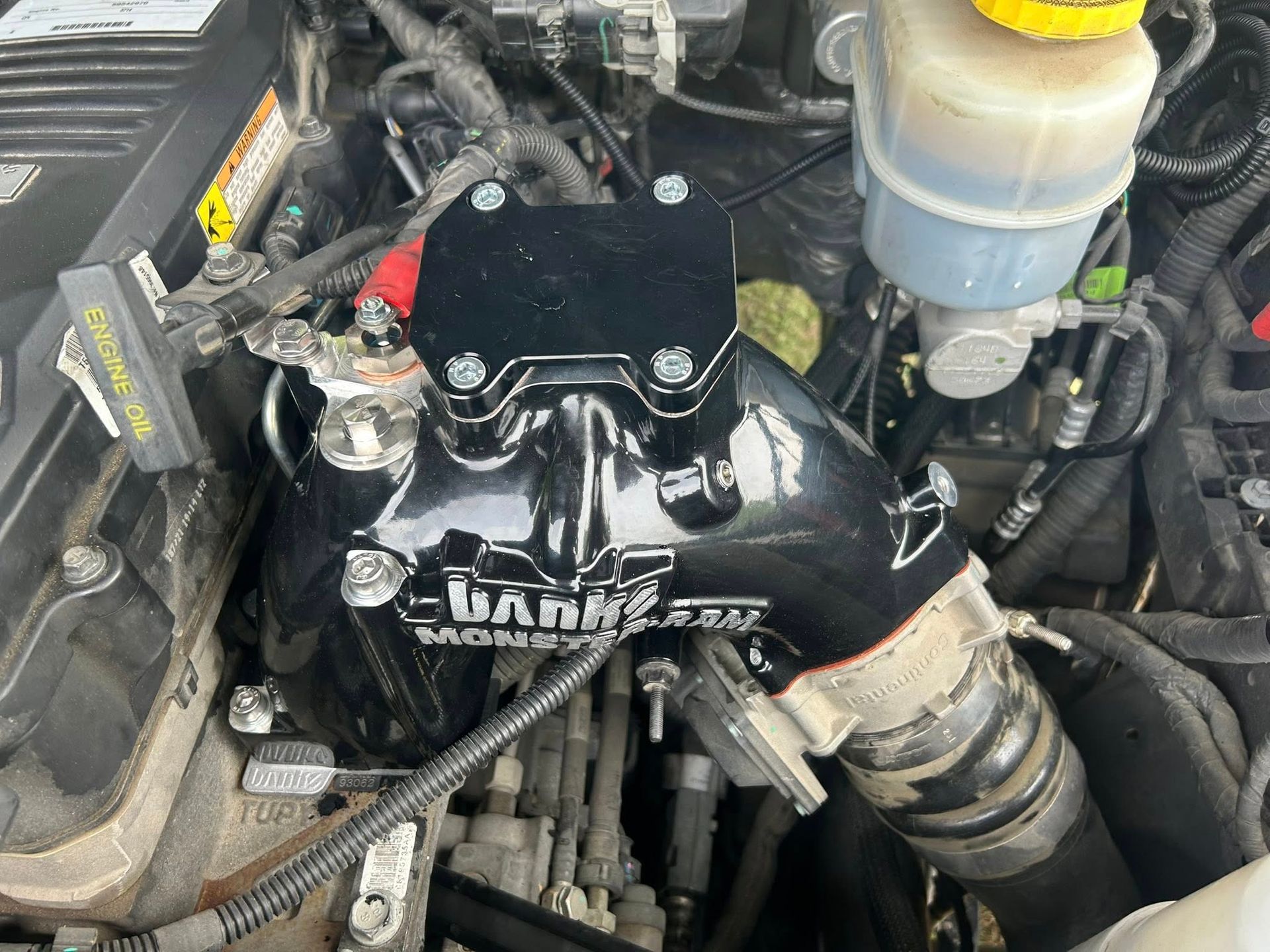 Car engine bay with black aftermarket intake piping and a translucent coolant reservoir.