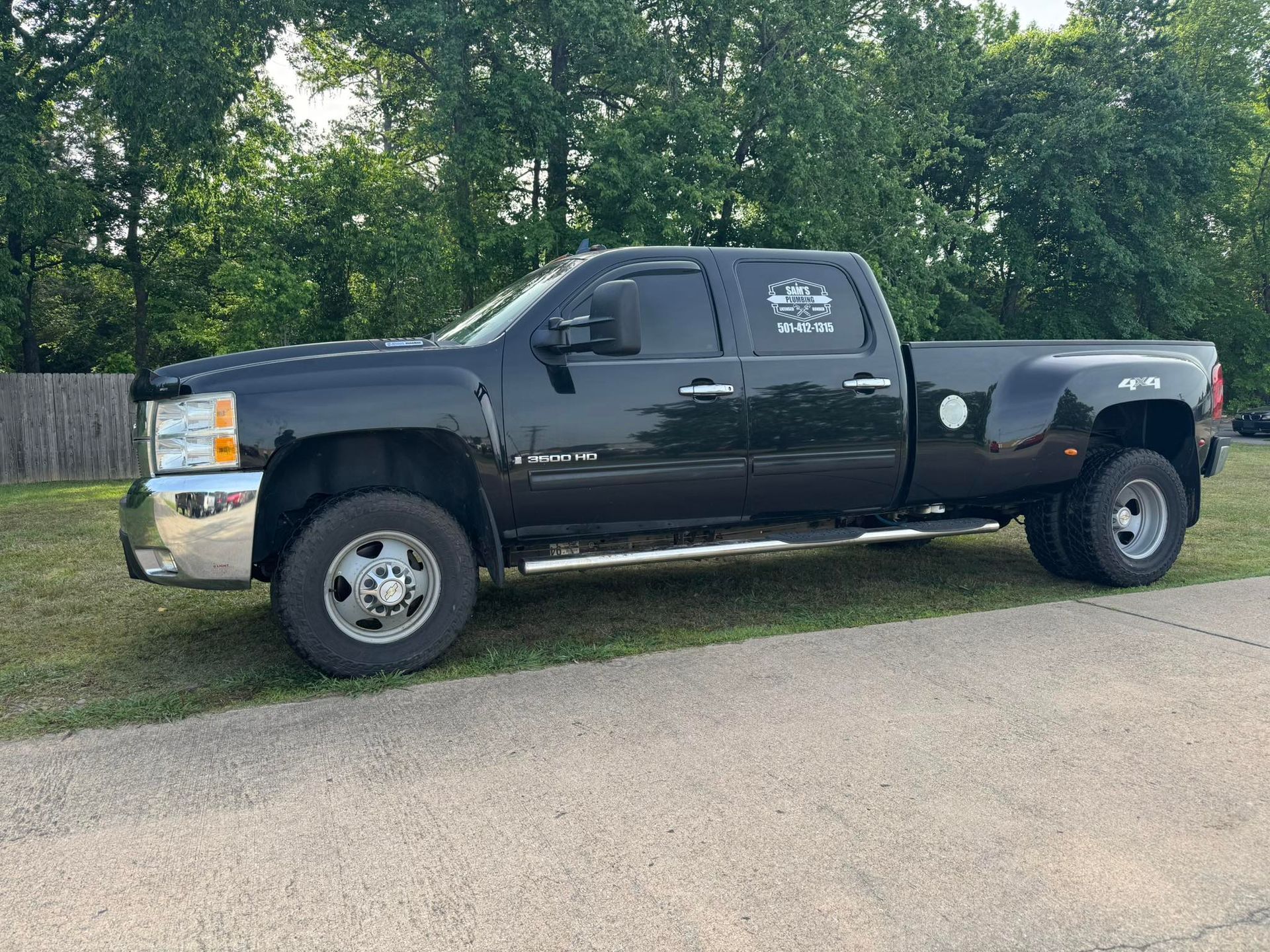 Black pickup truck parked on grass beside a road with trees in the background