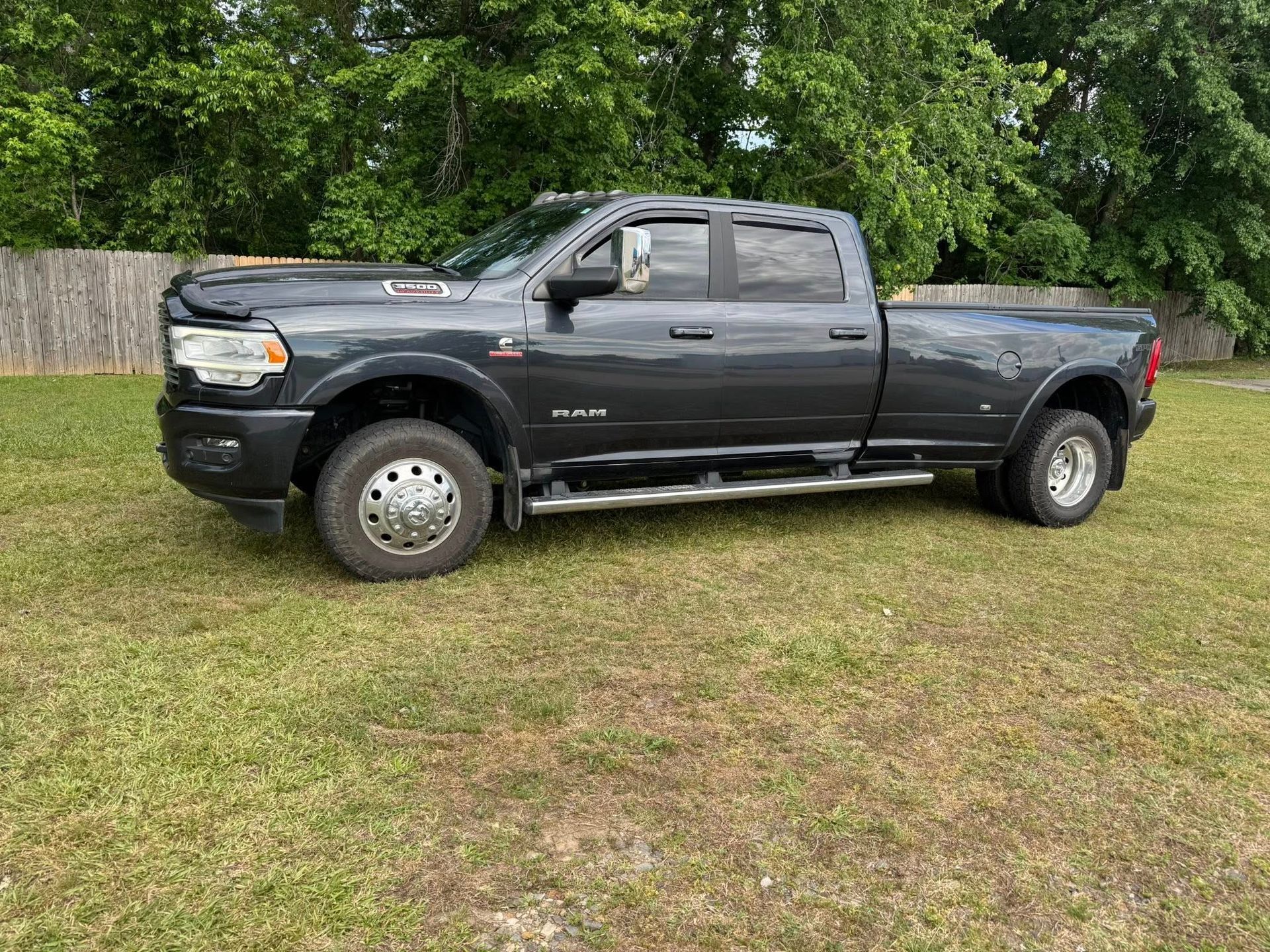 Dark gray pickup truck parked on grass in front of green trees