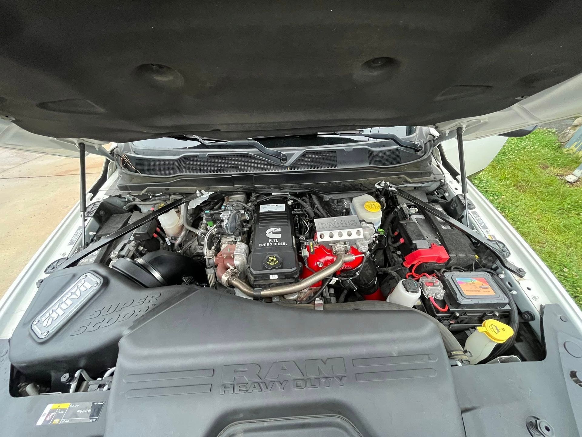 Car engine bay with hood open, showing black and red components and a battery on the right.
