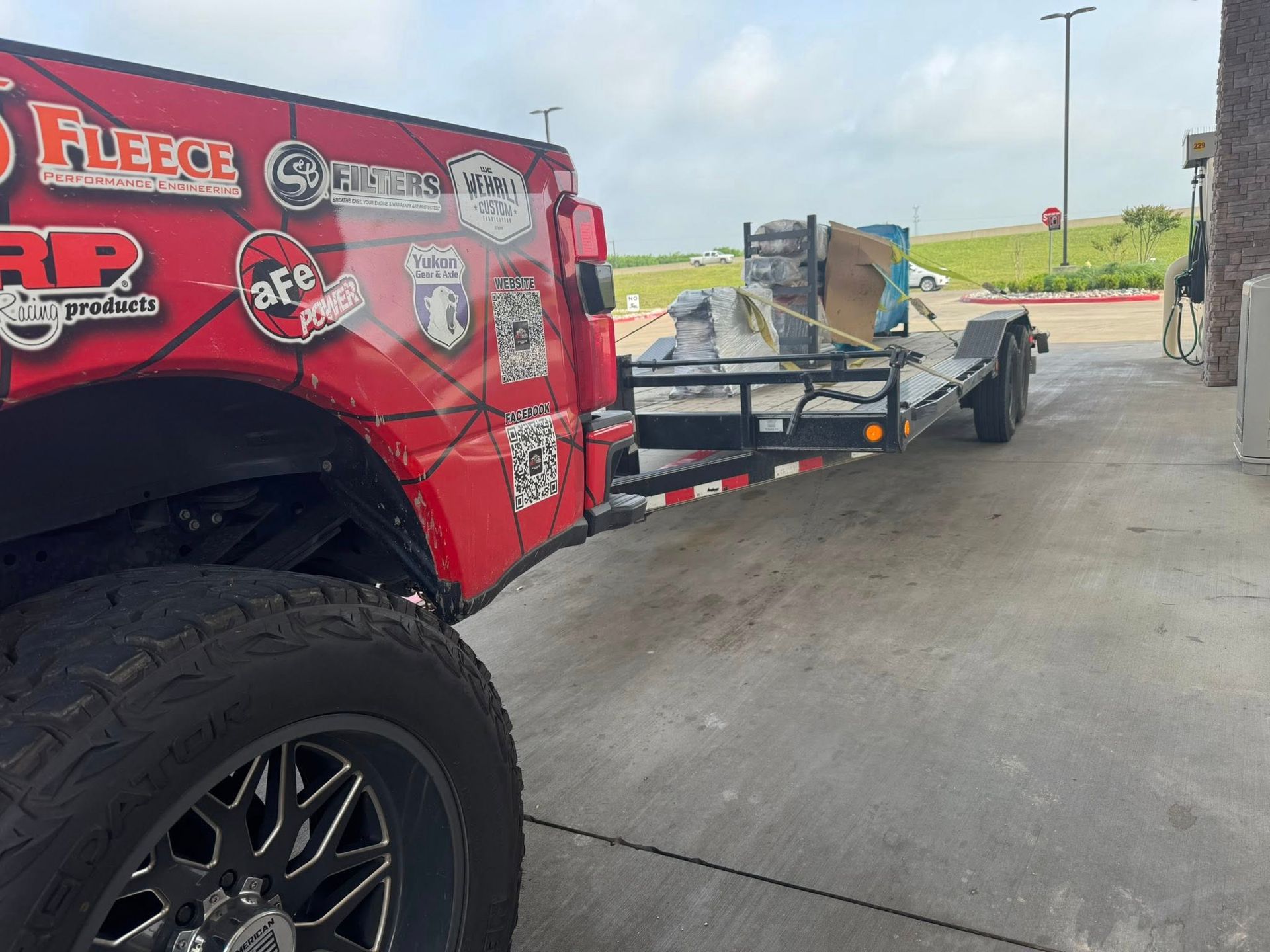 Red off-road truck towing a utility trailer at a gas station.
