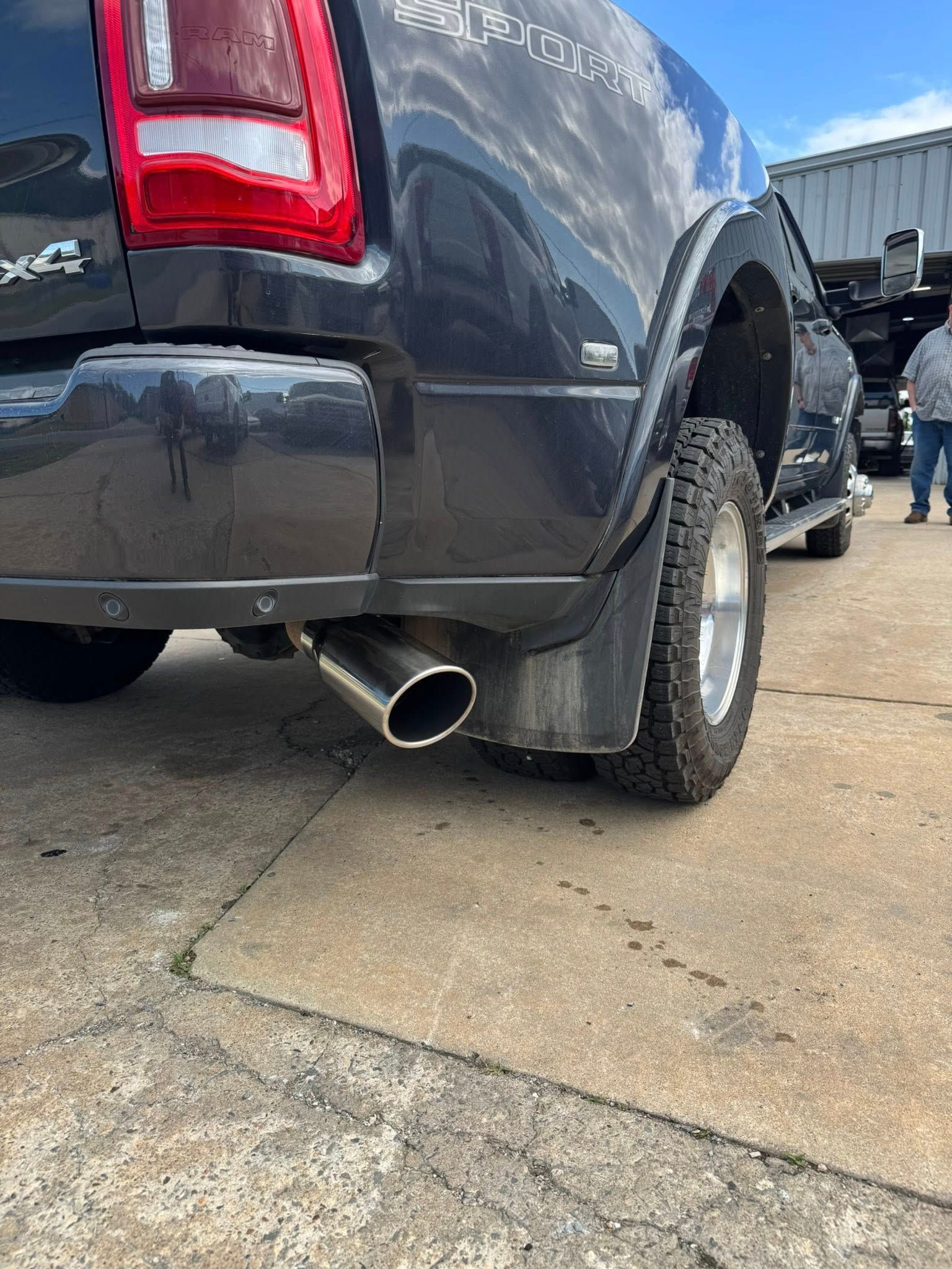 Black pickup truck rear wheel and chrome exhaust pipe on a concrete lot.