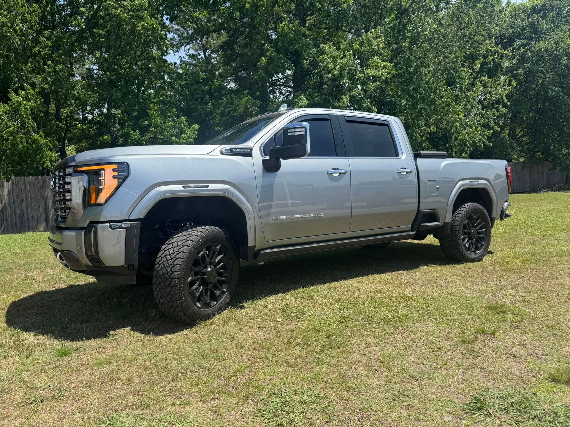 Silver pickup truck parked on grass in front of leafy trees
