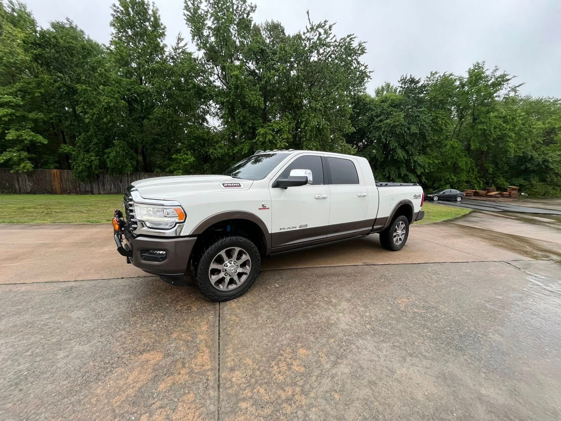 White lifted pickup truck parked on a gravel lot with trees in the background