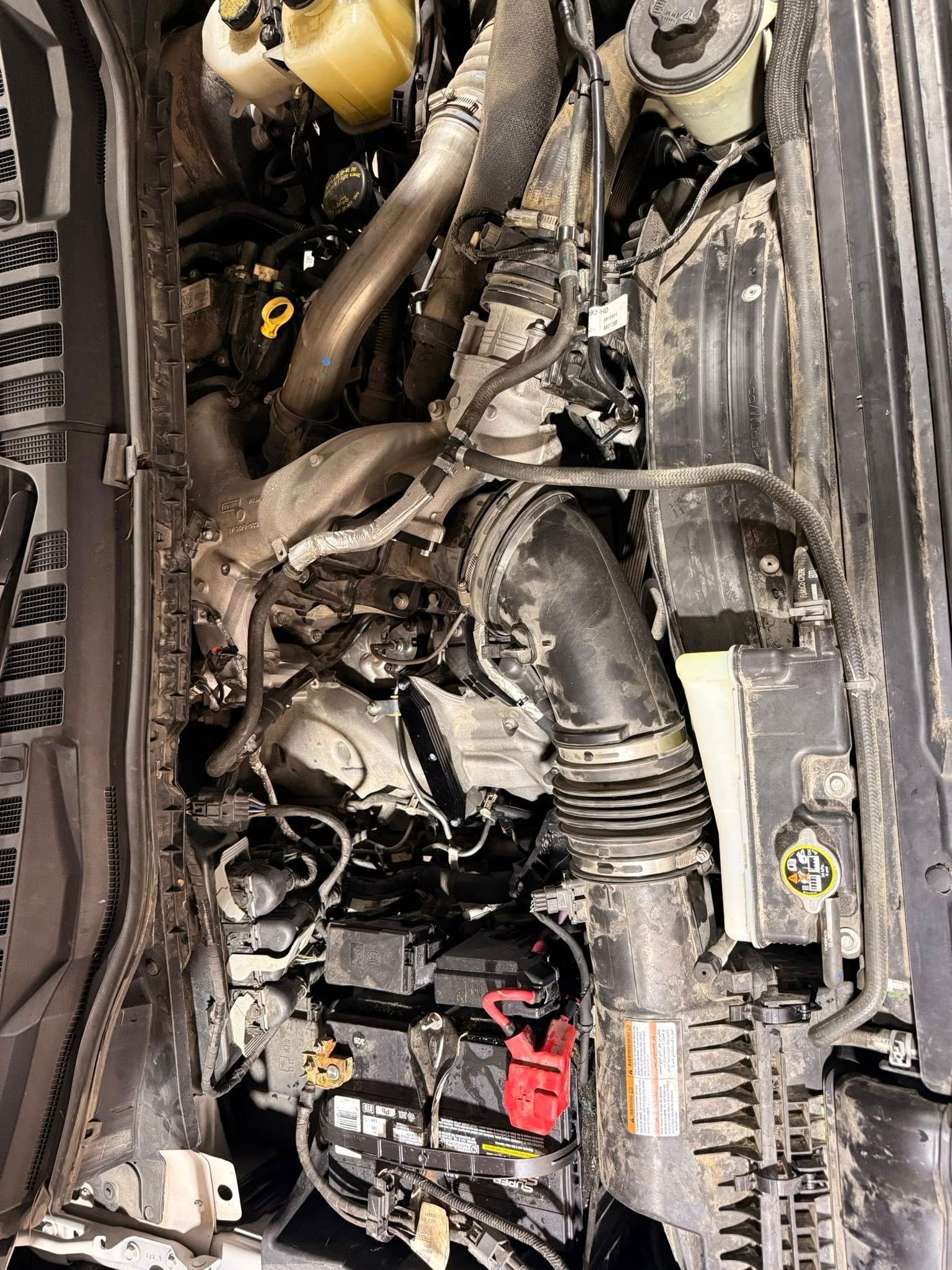 Close-up of an engine bay with hoses, wiring, and a red battery terminal.