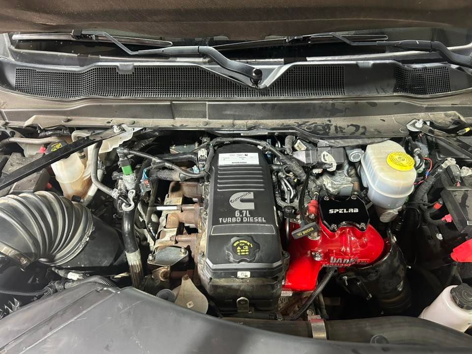 Open engine bay of a vehicle with a black engine cover, red engine parts, and a yellow fluid reservoir