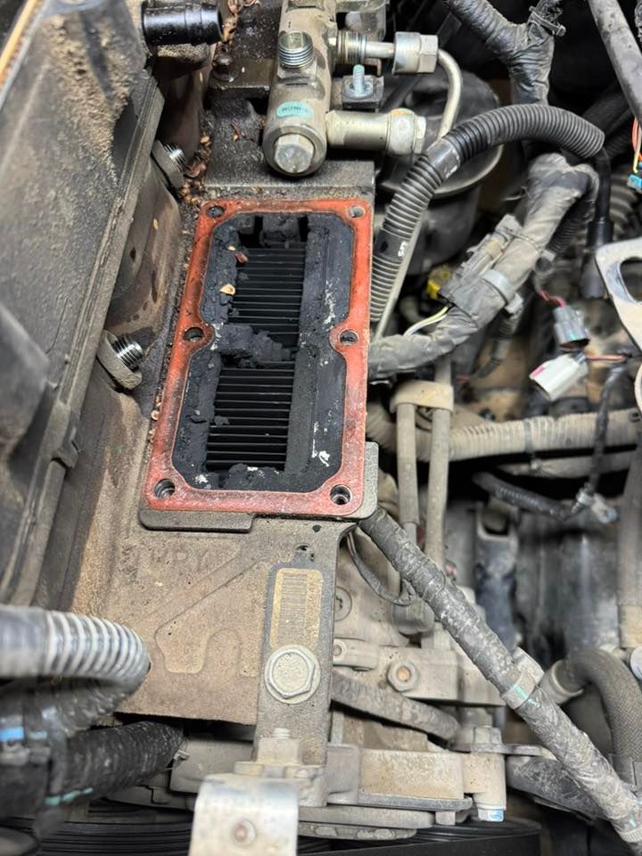 Close-up of a vehicle engine bay with an open red gasketed cover exposing a dark rectangular component.