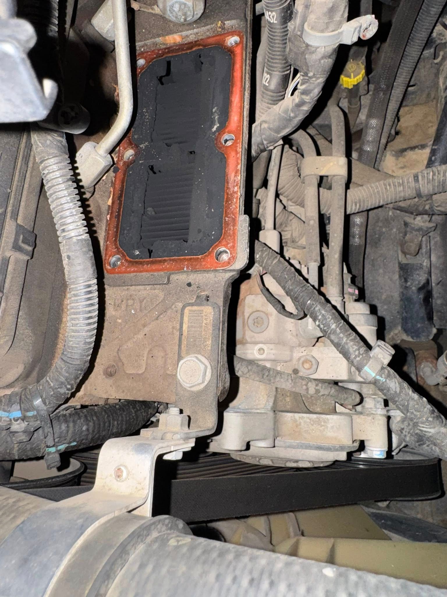 Close-up of a vehicle engine component with an orange gasket and dusty metal housing.