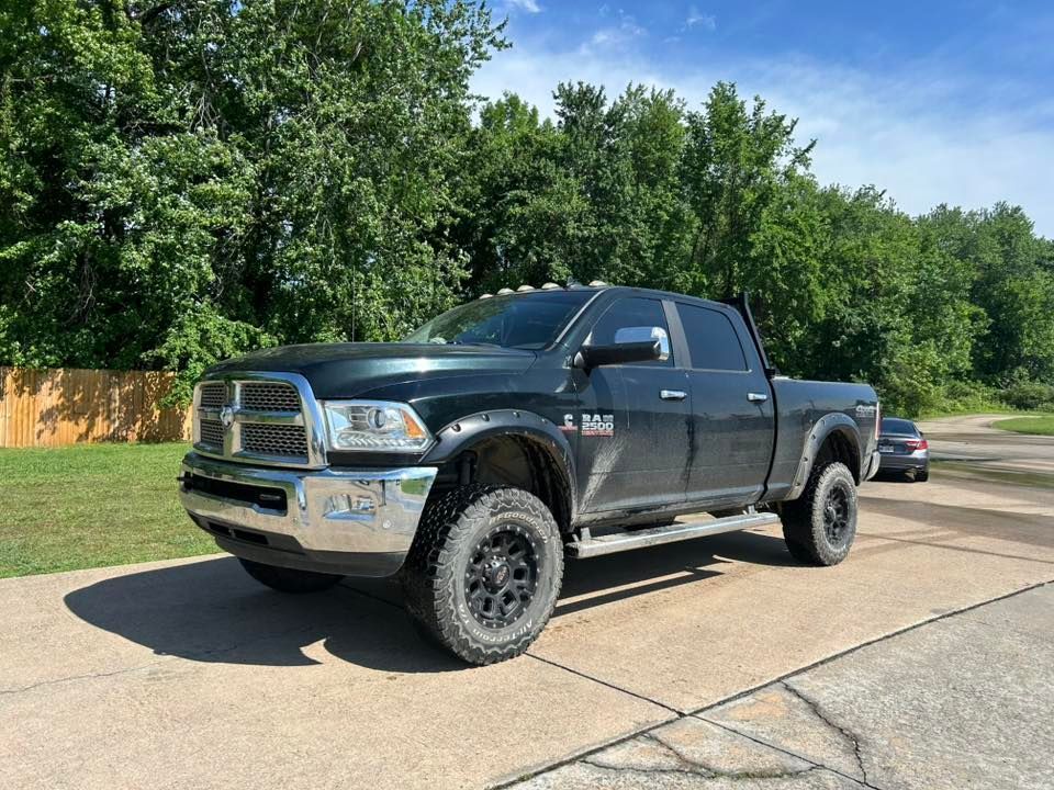 Black lifted Ram pickup parked on a sunny residential street with trees in the background