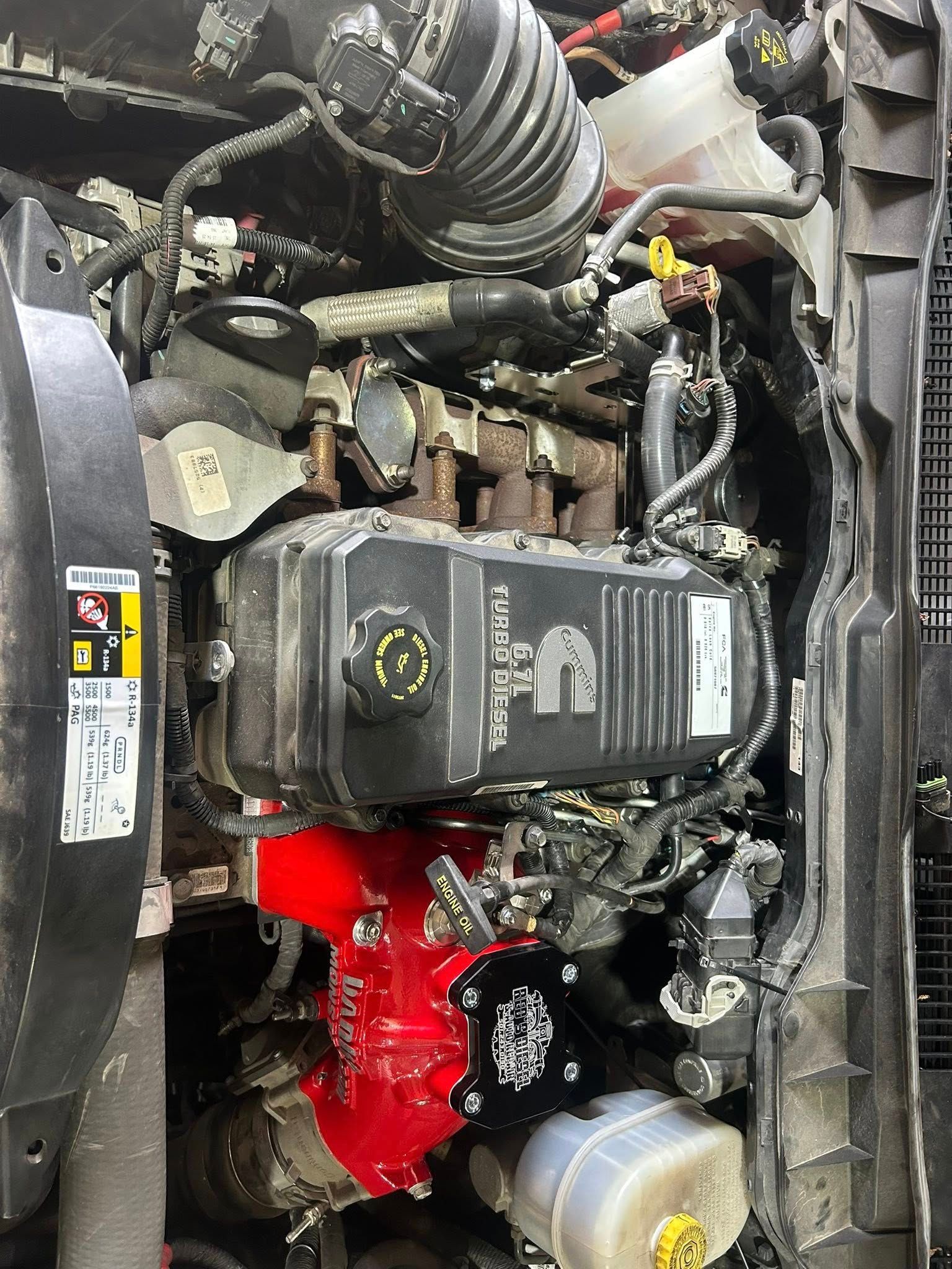 Car engine bay with black air intake, red engine cover, and visible hoses and battery components.