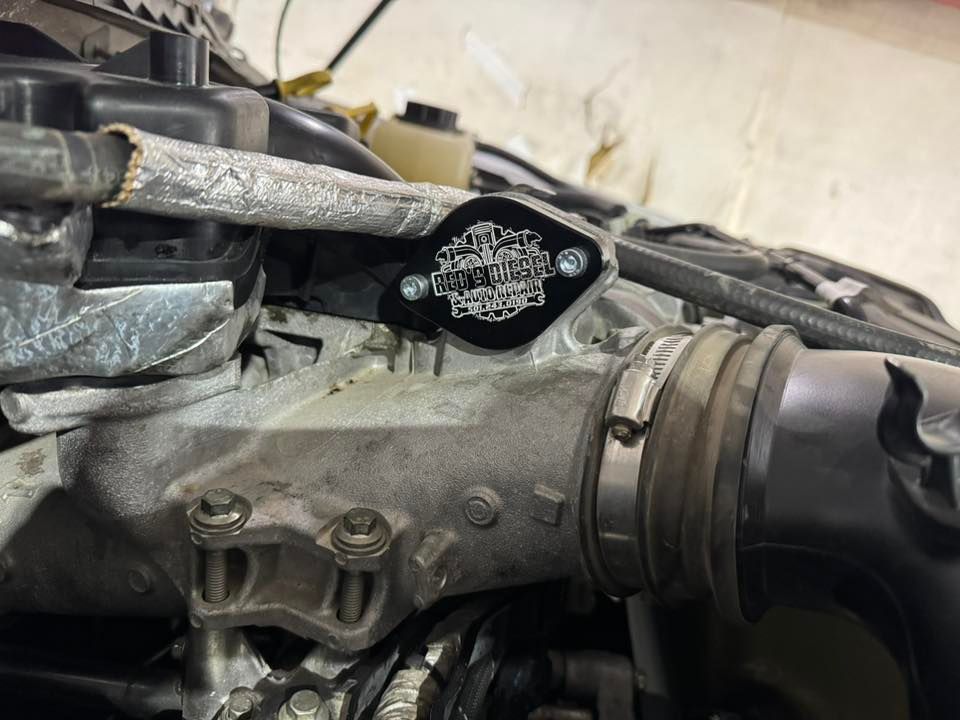 Close-up of a dirty engine component with a black aftermarket part mounted on top.