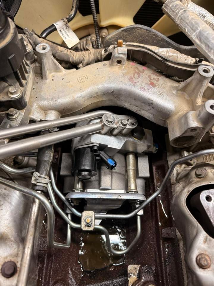 Close-up of an engine bay with exposed metal components and hoses, showing a leak or pooled fluid below.
