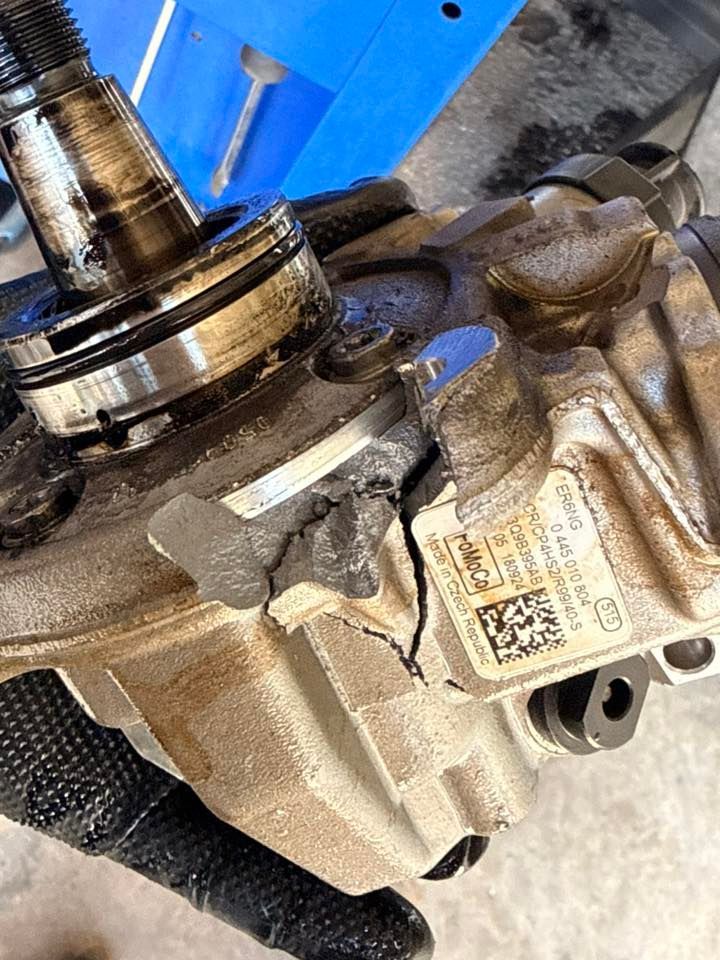 Close-up of a metal automotive mechanical part with a shaft, bolts, and identification label on a blue background