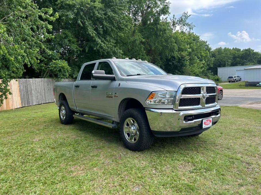 Silver pickup truck parked on grass beside a wooden fence and trees