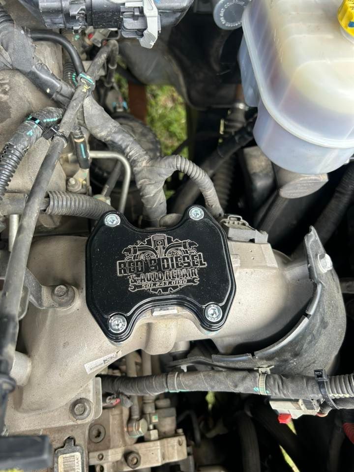 Engine bay with aftermarket black oil cap on a silver intake manifold, surrounded by hoses and wiring.