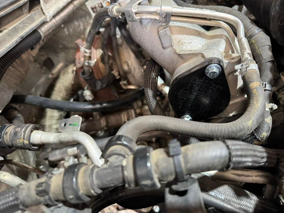 Close-up of an engine bay with hoses, wiring, and a black plastic component.
