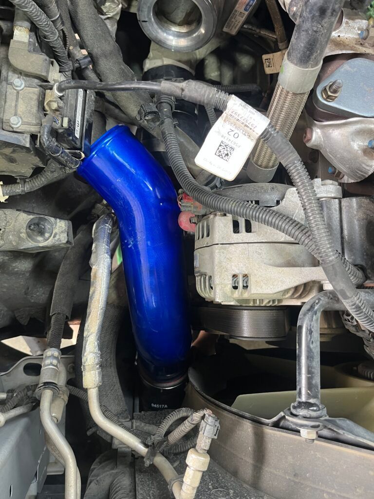 Blue aftermarket car intake pipe in an engine bay with hoses, wiring, and metal components.