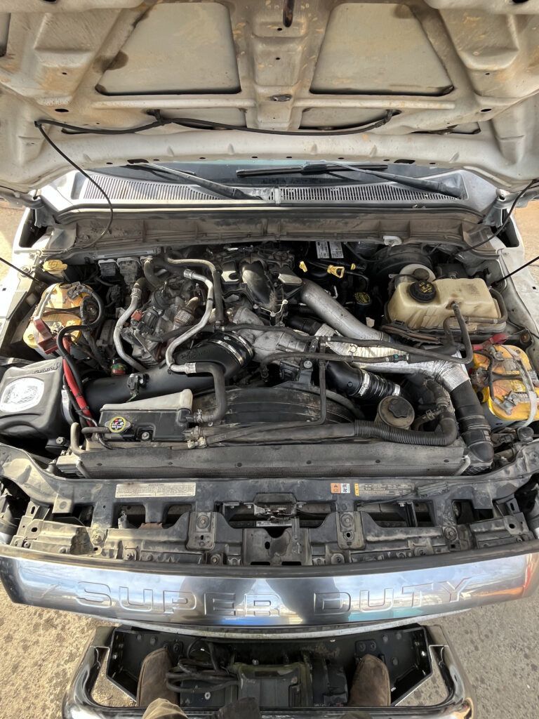 Open car hood showing a cluttered engine bay with hoses, wires, and exposed mechanical parts.