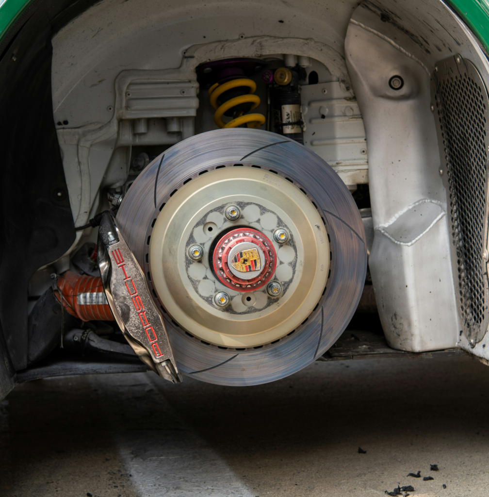 Close-up of a car wheel and brake assembly inside a wheel well, with a yellow suspension spring above.