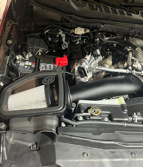 Car engine bay with a black air intake and red battery cover