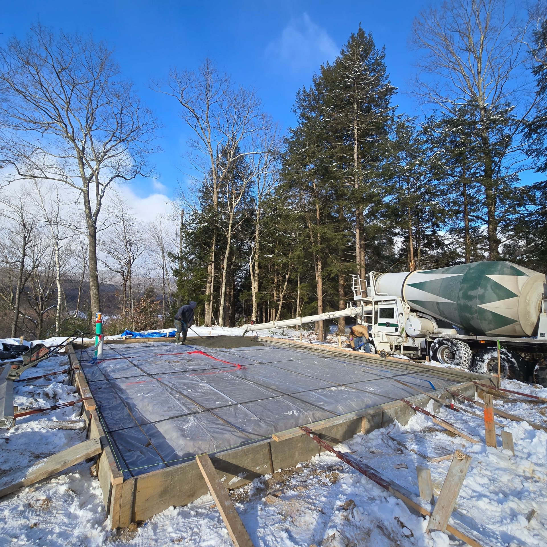 A concrete truck is pouring concrete into a foundation in the snow.