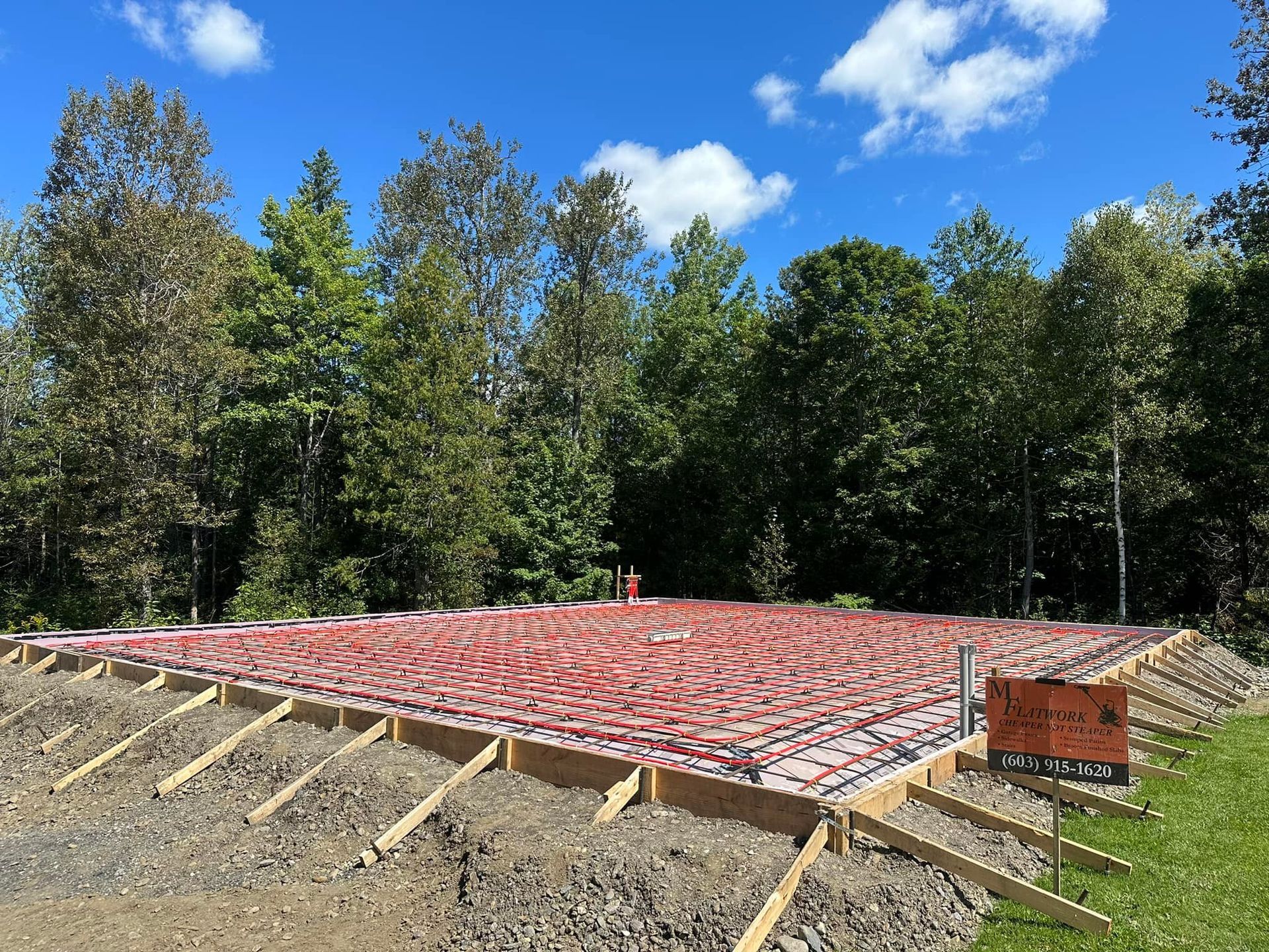 A foundation for a house is being built in a yard with trees in the background.