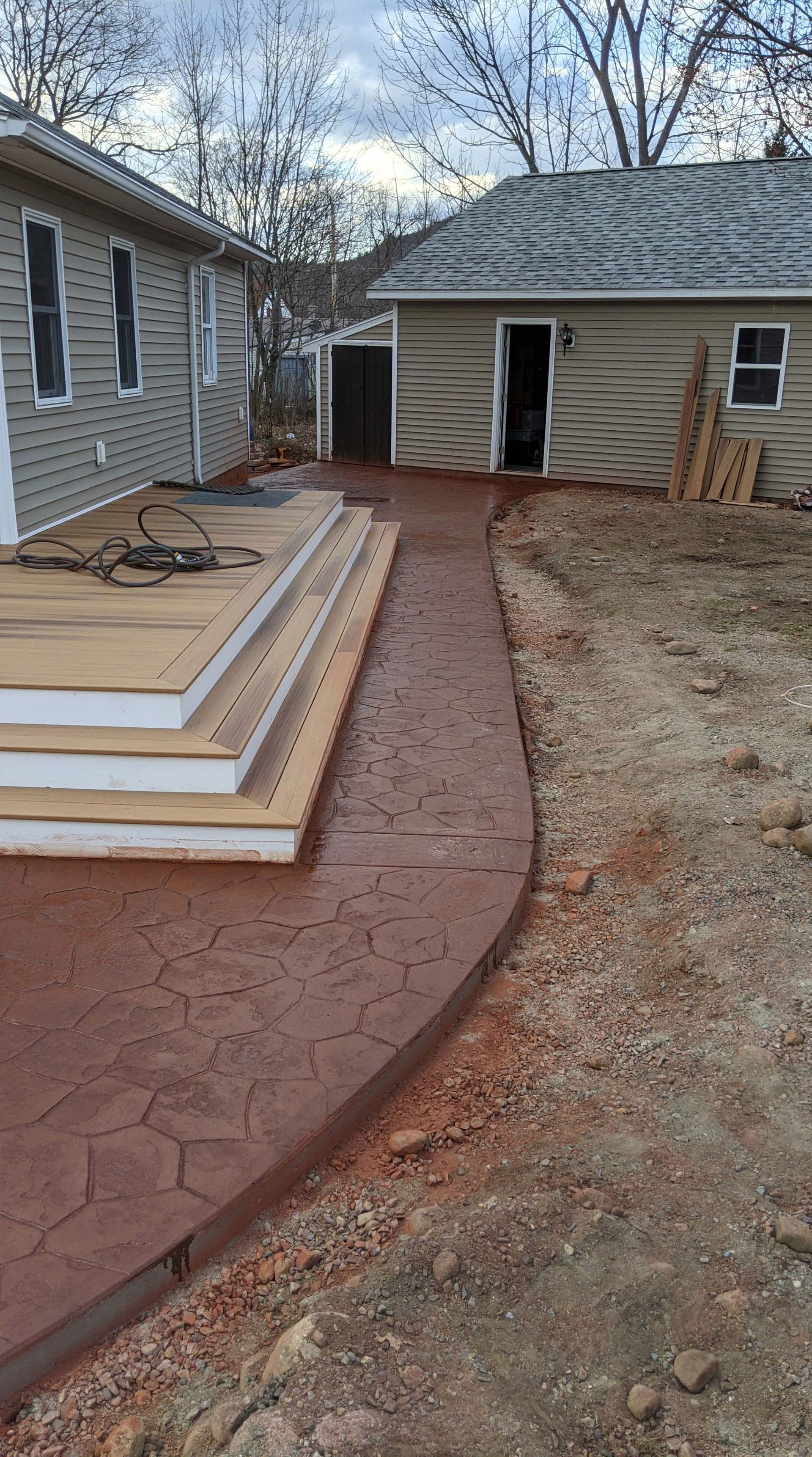 A reddish-brown stamped concrete walkway leading to the steps of a gray house exterior, next to a detached garage.