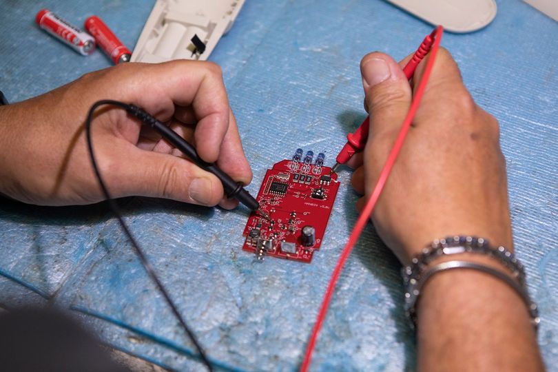 Hands soldering a small red circuit board on a blue work surface