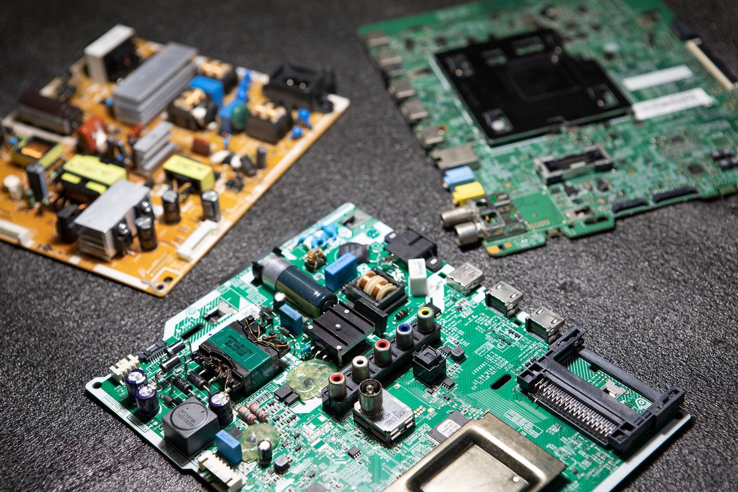 Three exposed computer circuit boards on a dark surface, including a green motherboard in the foreground.