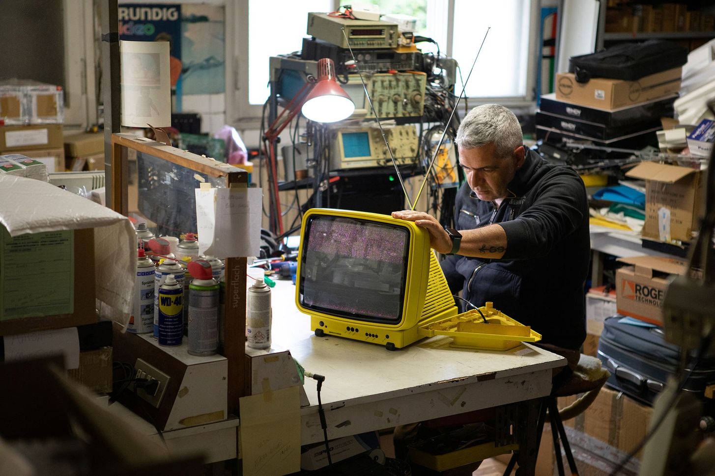 Person working on a yellow CRT television in a cluttered workshop