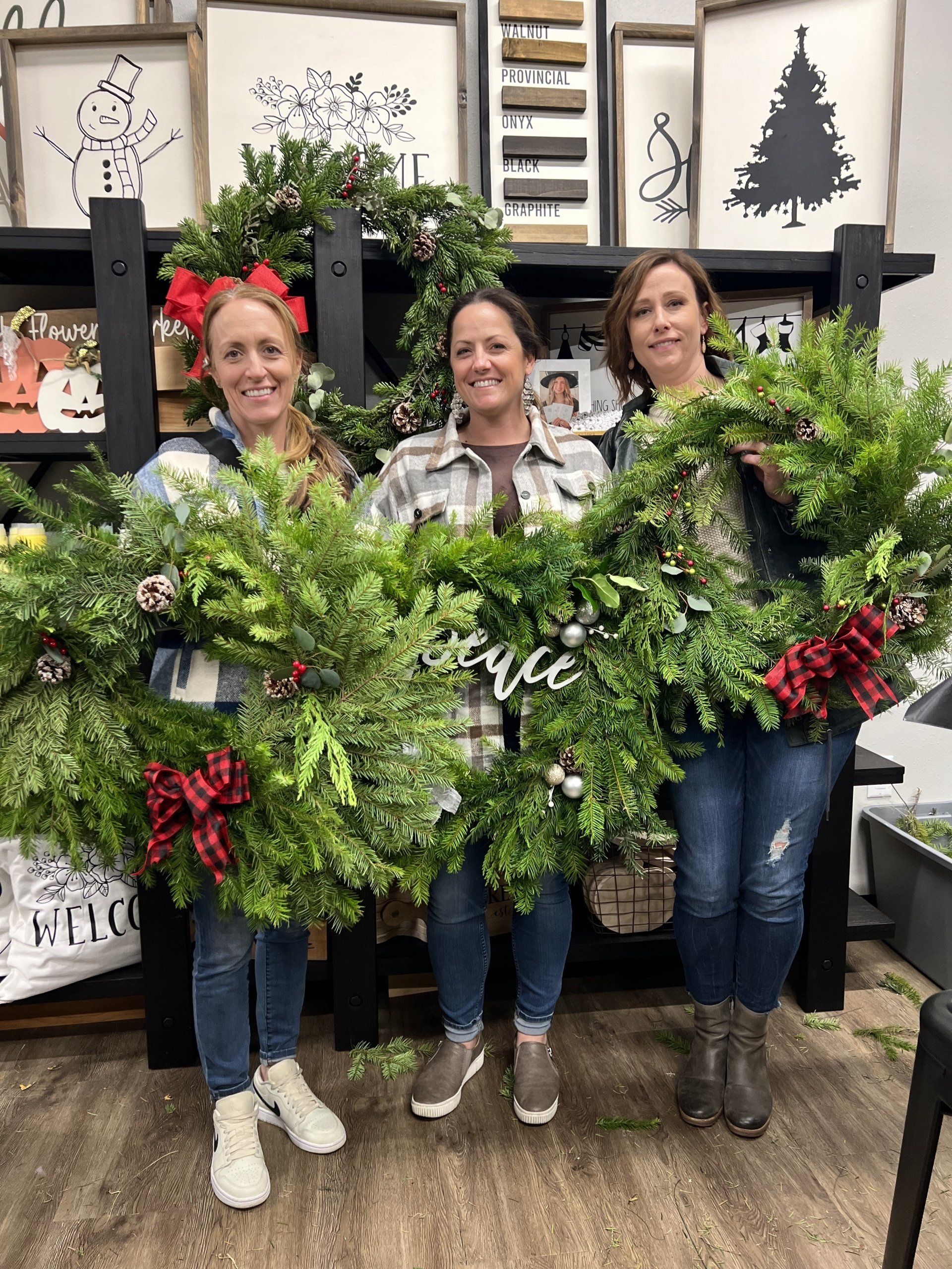 Three women are holding christmas wreaths in a room.