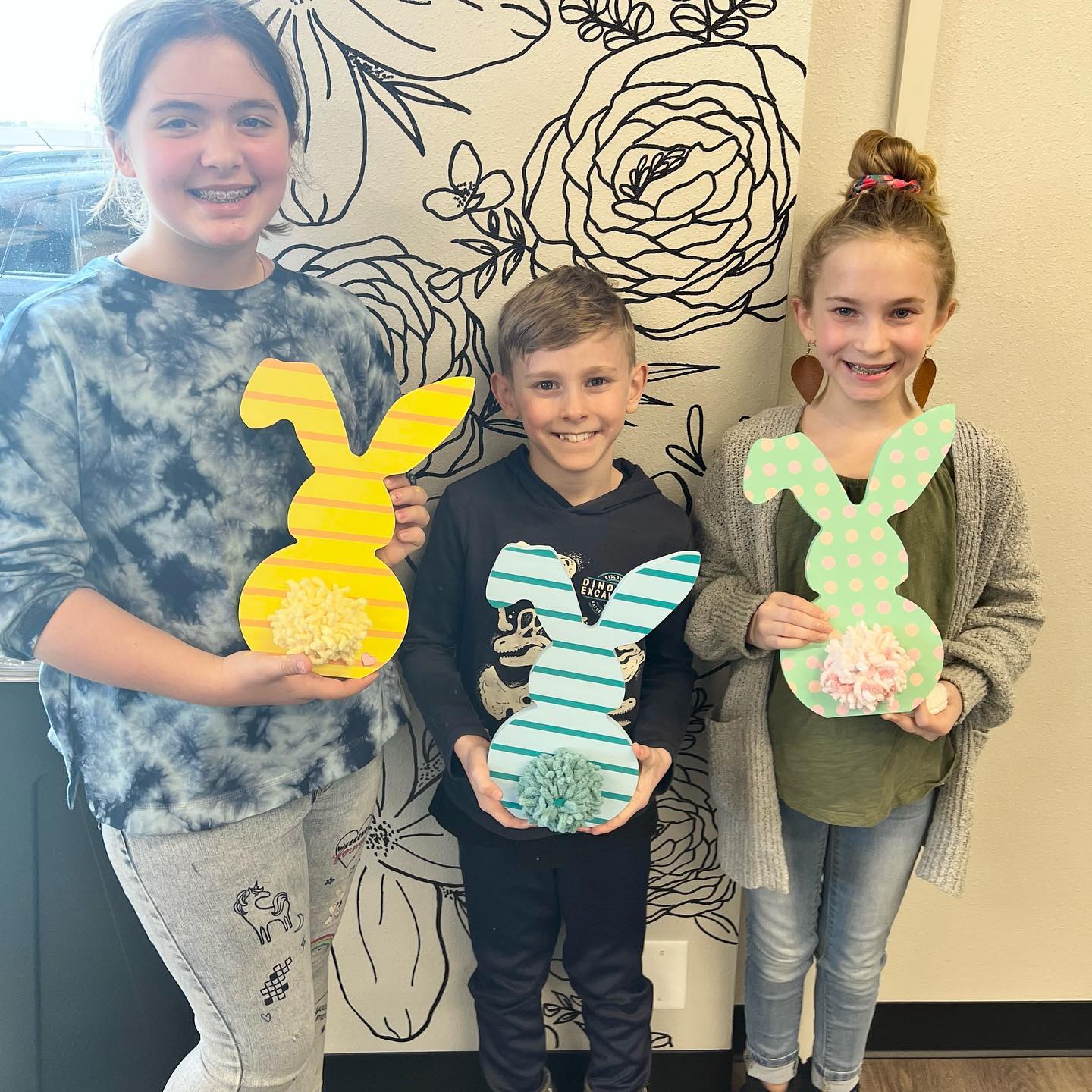 Three children are standing next to each other holding easter bunny crafts.