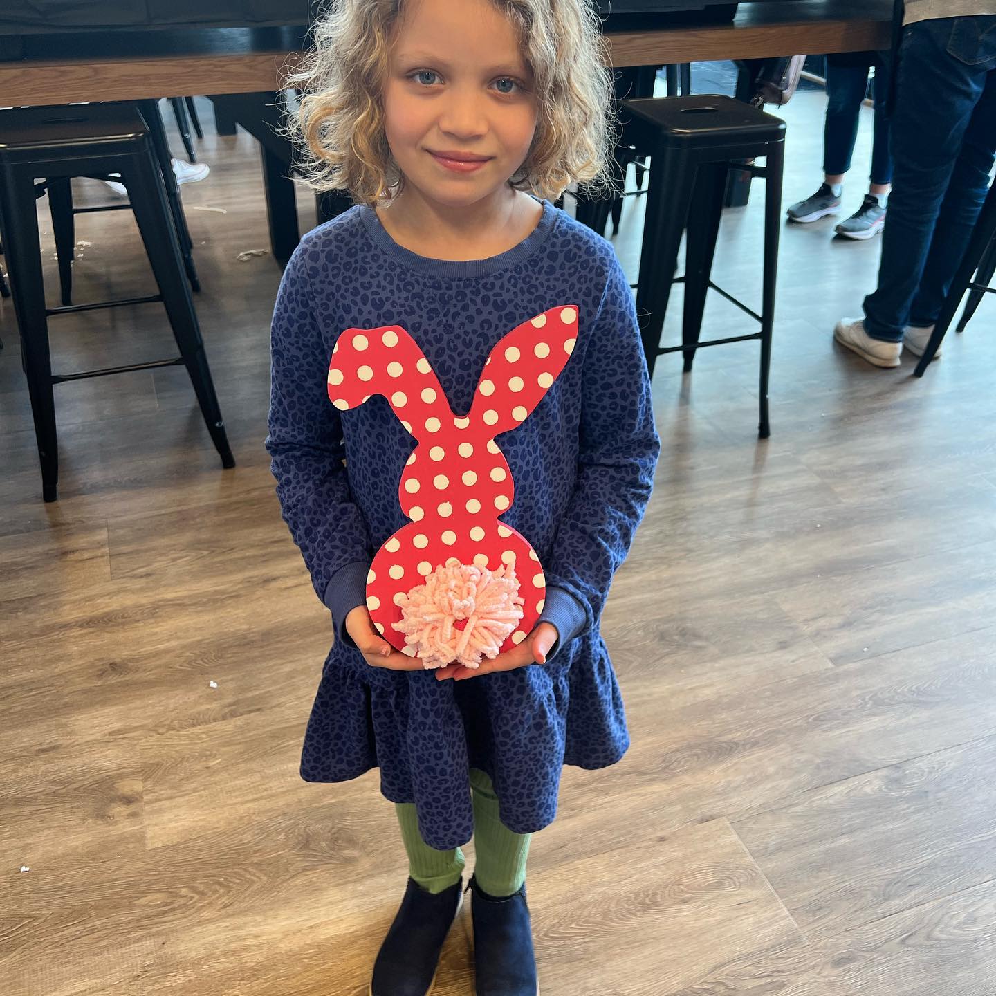 A little girl in a blue dress is holding a red and white polka dot bunny