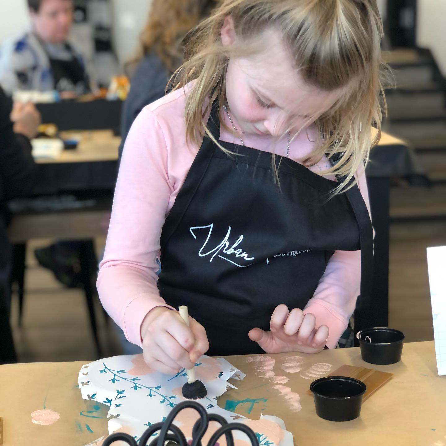 A little girl wearing an apron that says urban on it
